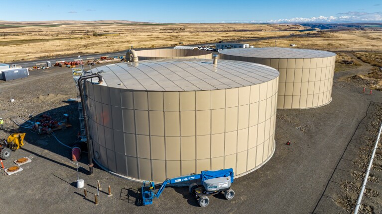 Large cylindrical storage tanks in arid landscape with construction equipment