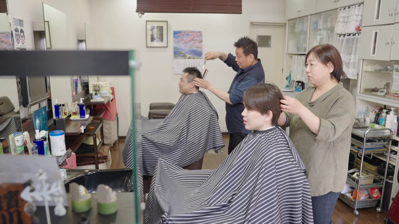理容室の店内でお客さんの髪を整えている美穂さん。その奥には別のお客様の髪を整えている夫の雄一さん