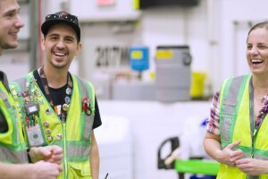 An image of Sarah Rhoads standing inside a fulfillment center with two other Amazon employees talking and laughing.