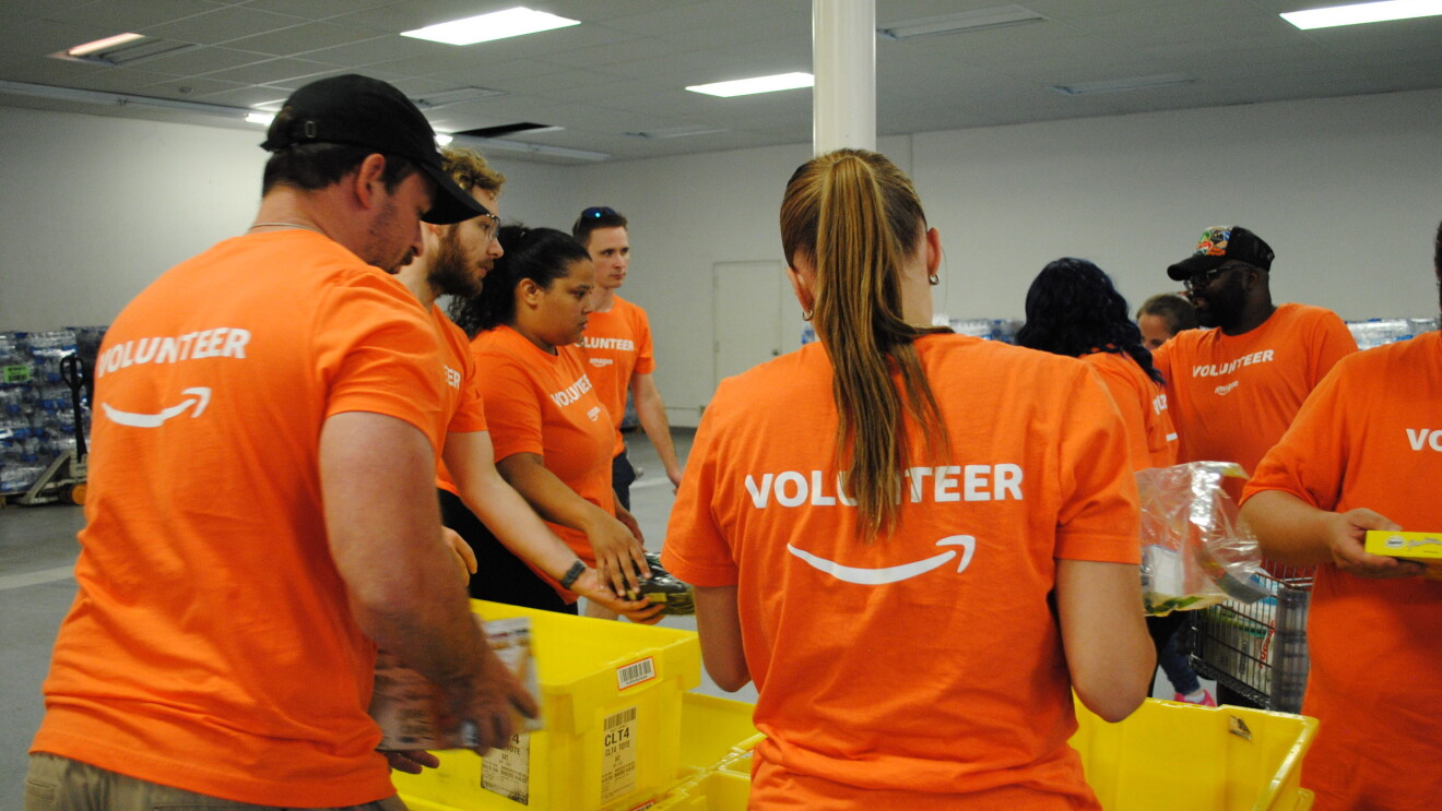 Amazon volunteers in orange shirts working together at a distribution center