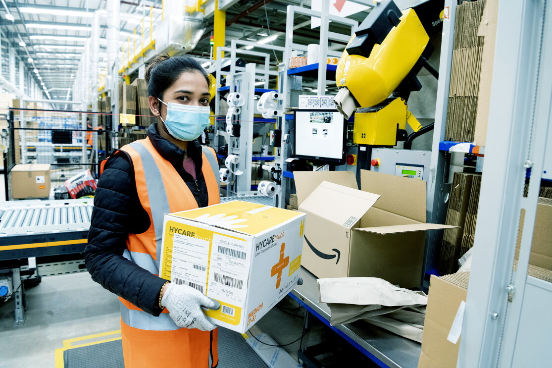 An Amazon employee at Coalville fulfillment center packs boxes with medical supplies to be sent to relevant government centers. She is wearing protective gloves and a face mask. 