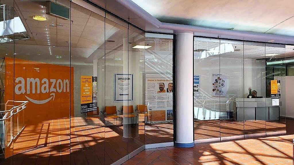 Ein mit Glas eingefasstes Bürogebäude von außen: Man sieht Amazon Poster und Logos sowie die weiße Empfangstheke