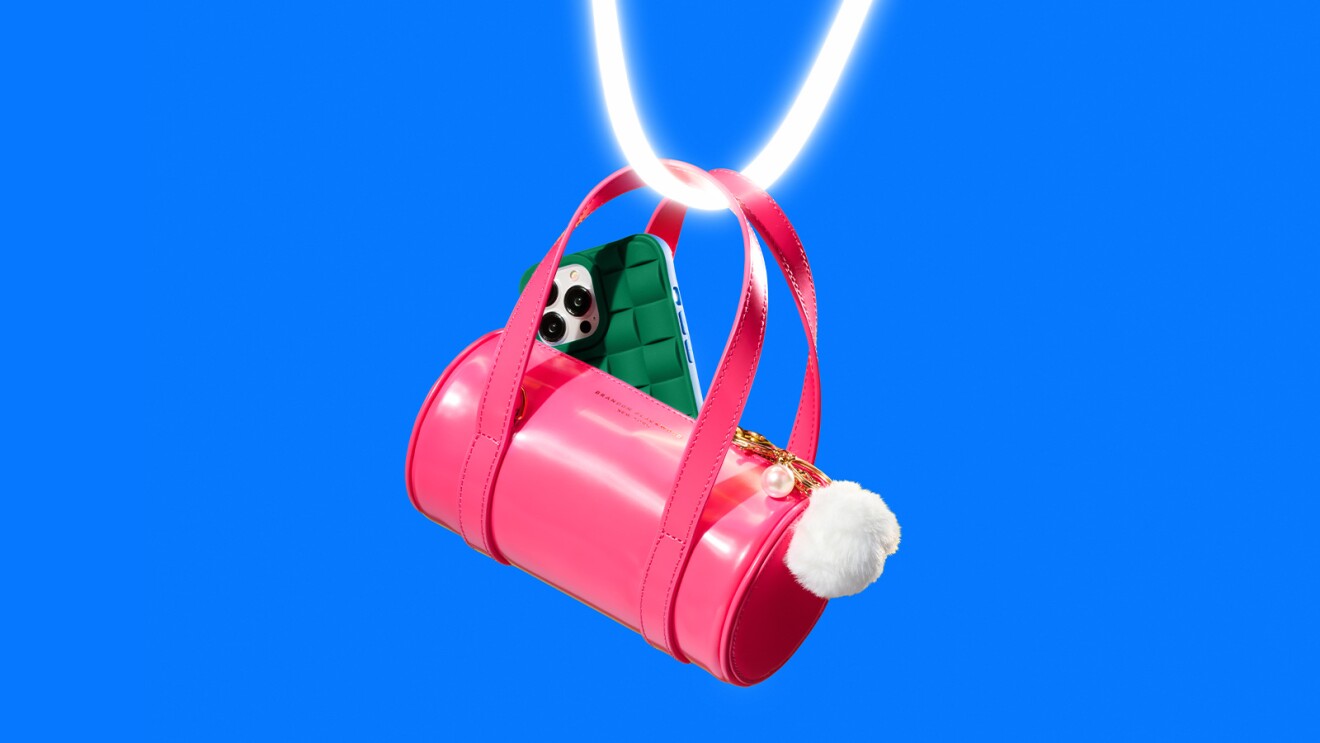 Pink cylindrical handbag suspended against blue background, partially revealing green smartphone