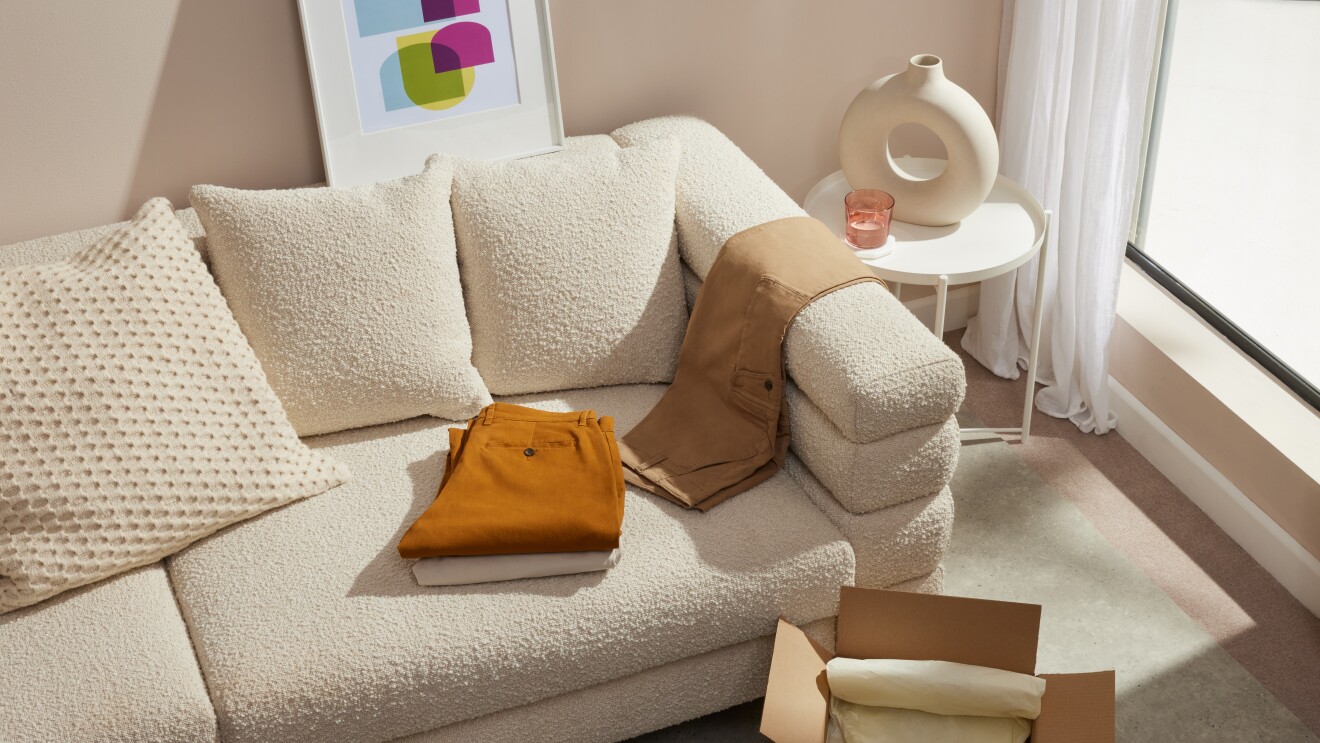 Gerade bei Hosen ist die richtige Länge und Passform wichtig. Das Bild zeigt eine geöffnete Amazon Versandbox mit drei Hosen in weiß, beige und braun, ausgebreitet auf einem hellen Sofa.