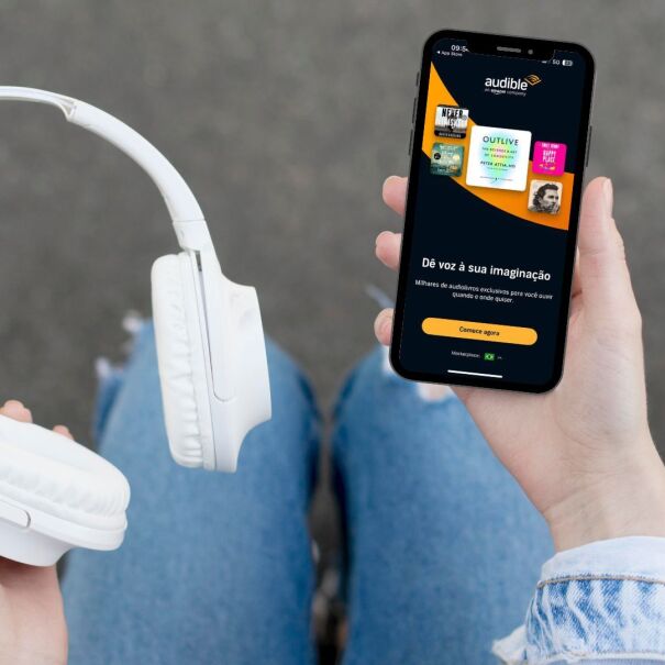 Um mulher segura um fone sem fio e um celular, com o aplicativo de Audible aberto