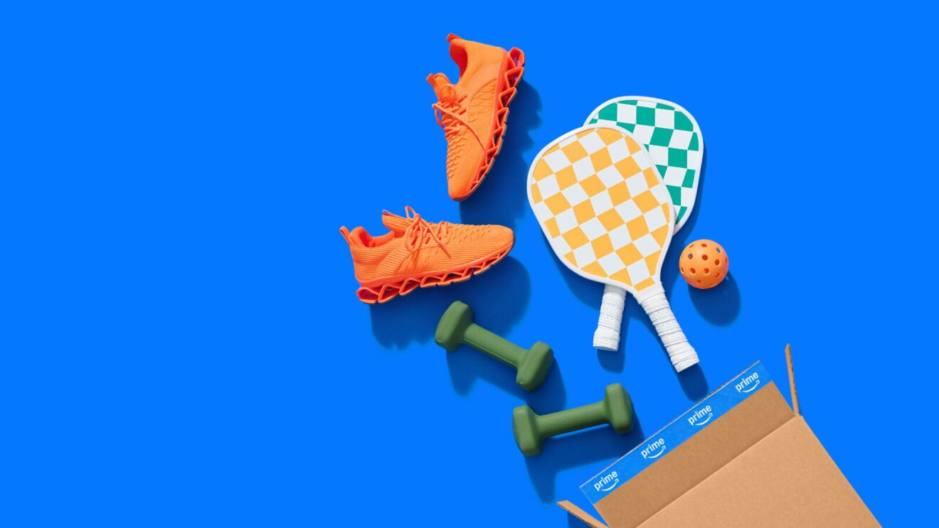 Orange athletic shoes, green dumbbells, pickleball paddles and ball spilling from Amazon Prime box on blue background