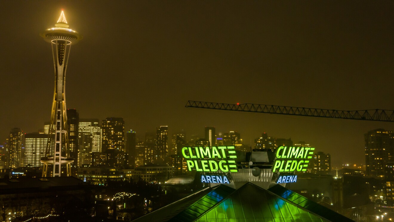 The Climate Pledge Arena signage lit up, with Seattle's Space Needle and skyline showing behind it.