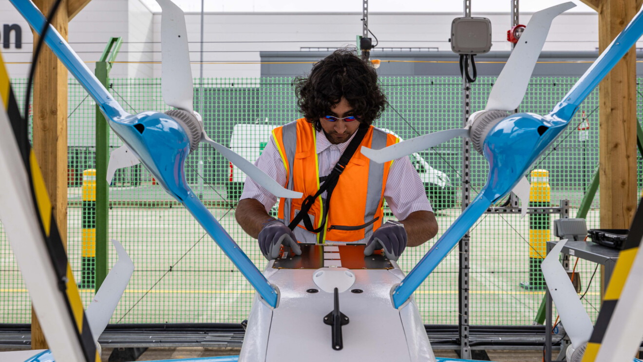 Amazon worker in safety vest performing maintenance on delivery drone in warehouse facility