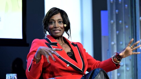 Sentada en un escenario aparece Bisila Bokokoemprendedora, escritora y filántropa hispano-estadounidense, Está sentada en una silla gris y negra. De fondo una pantalla donde aparecen sus nombres y sus cargos y el nombre del programa Mujeres Que Rompen barreras. Bisila va con una falda negra imitación piel, un blazer de color negro y una americana roja, con motivos blancos y negros. Bisila es afrodescendiente.