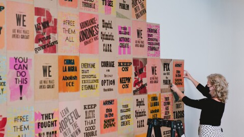 一位艺术家戴着面具,把几十张宣传单式的海报挂在墙上。