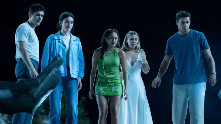 Ensemble cast stare down towards the ground during the night