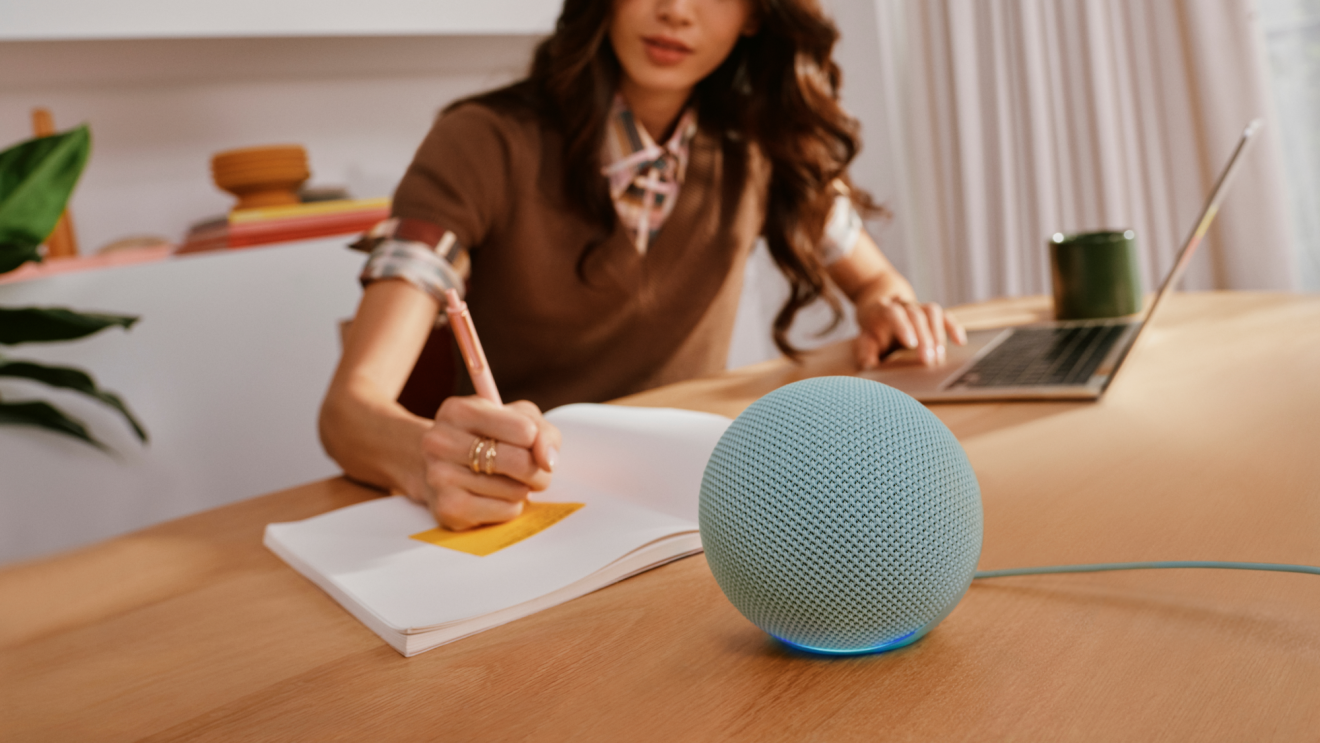 A person working at a desk with their laptop devices, notepad, and Echo Dot.