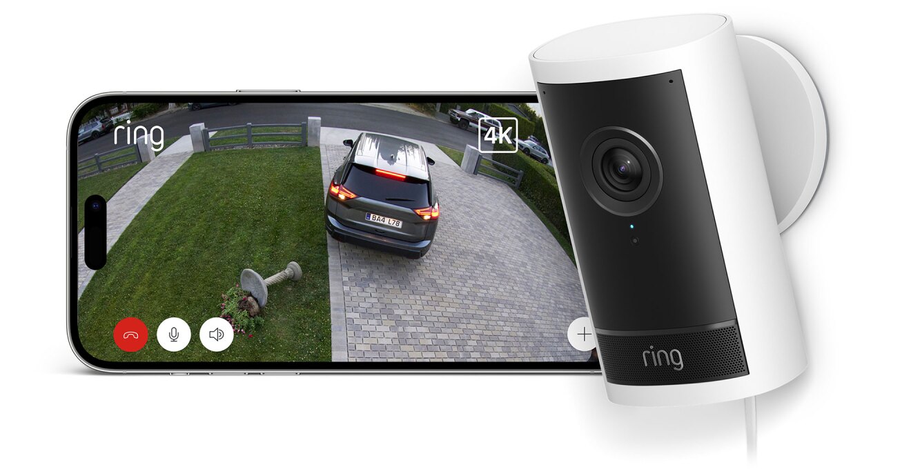 カメラの映像を表示する横長のディスプレイ、右側に白い円柱状筐体の監視カメラ。画面には石畳のアプローチと芝生の前庭が映っている。黒い乗用車がバックで芝生の上の花台を倒した様子。