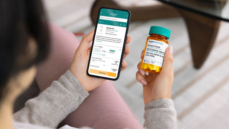 Hands holding smartphone displaying Amazon Pharmacy app and medication bottle