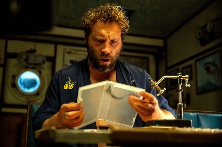 Jai Courtney sits at his desk inside a boat