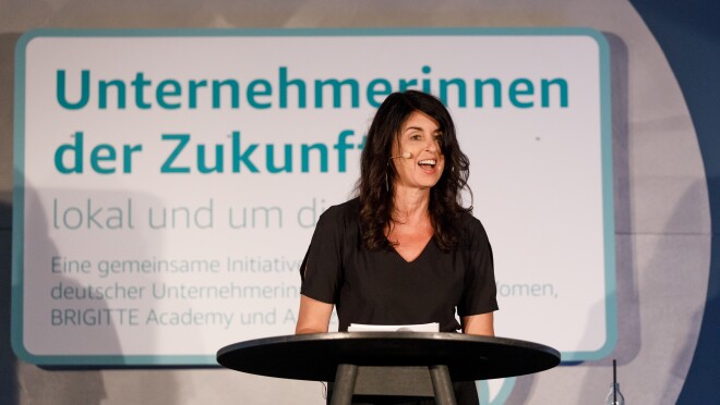 Brigitte Huber steht auf de Bühne am Rednerpult, sie hält eine Laudatio und verkündet die Gewinnerin