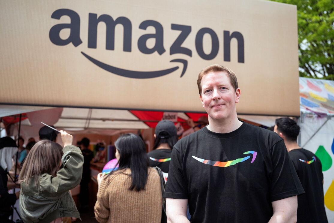 Amazonと書かれたブースの前に立つ黒いTシャツを着た背の高い男性