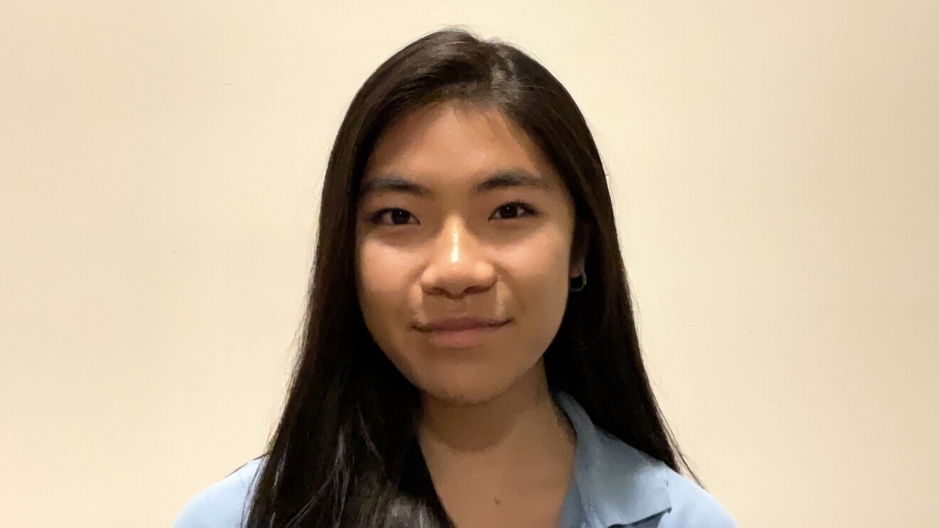 A headshot image of a young woman. There is a white wall in the background behind her.