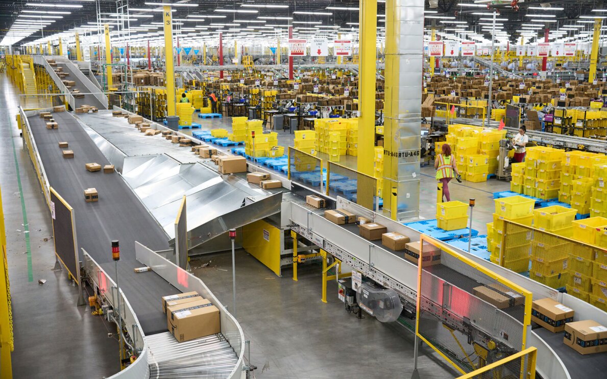 A photo of the inside of an Amazon fulfillment center showing many packages on a conveyor belt and being sorted in the background.