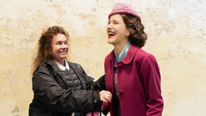 一个女人正在给一个女演员缝补一件戏服的形象。两人都在微笑和大笑。