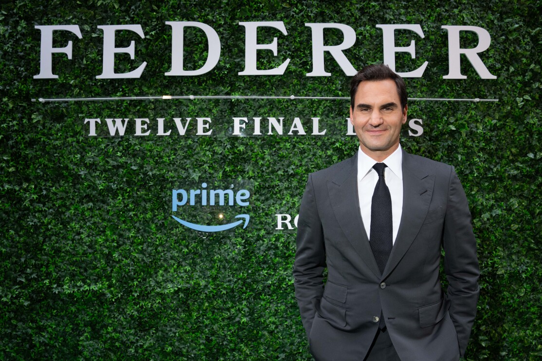Tennis star Roger Federer in a black suit standing in front a grass wall background