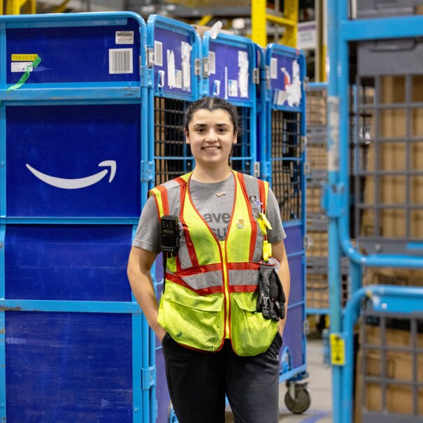Amazon employee in safety vest smiling next to blue delivery carts