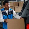 An Amazon volunteer at a food bank, loading a box of groceries into a car.