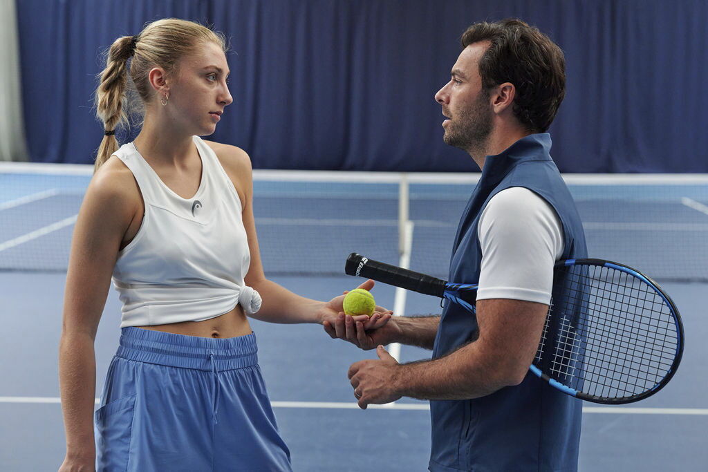 Justine and Glenn speak on a tennis court