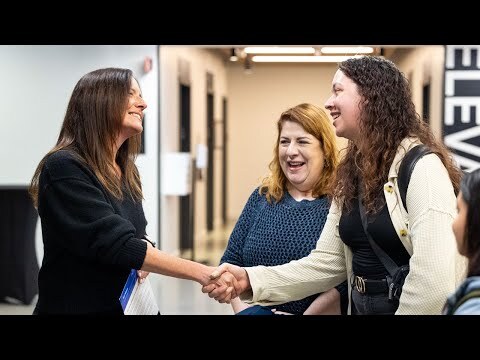 An image of Amazon's Senior Vice President of People Experience, Beth Galetti, shaking hands with employees in a hallway and smiling.