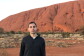 A man wearing a half-zip jacket and t-shirt stands in an arid location near the brush