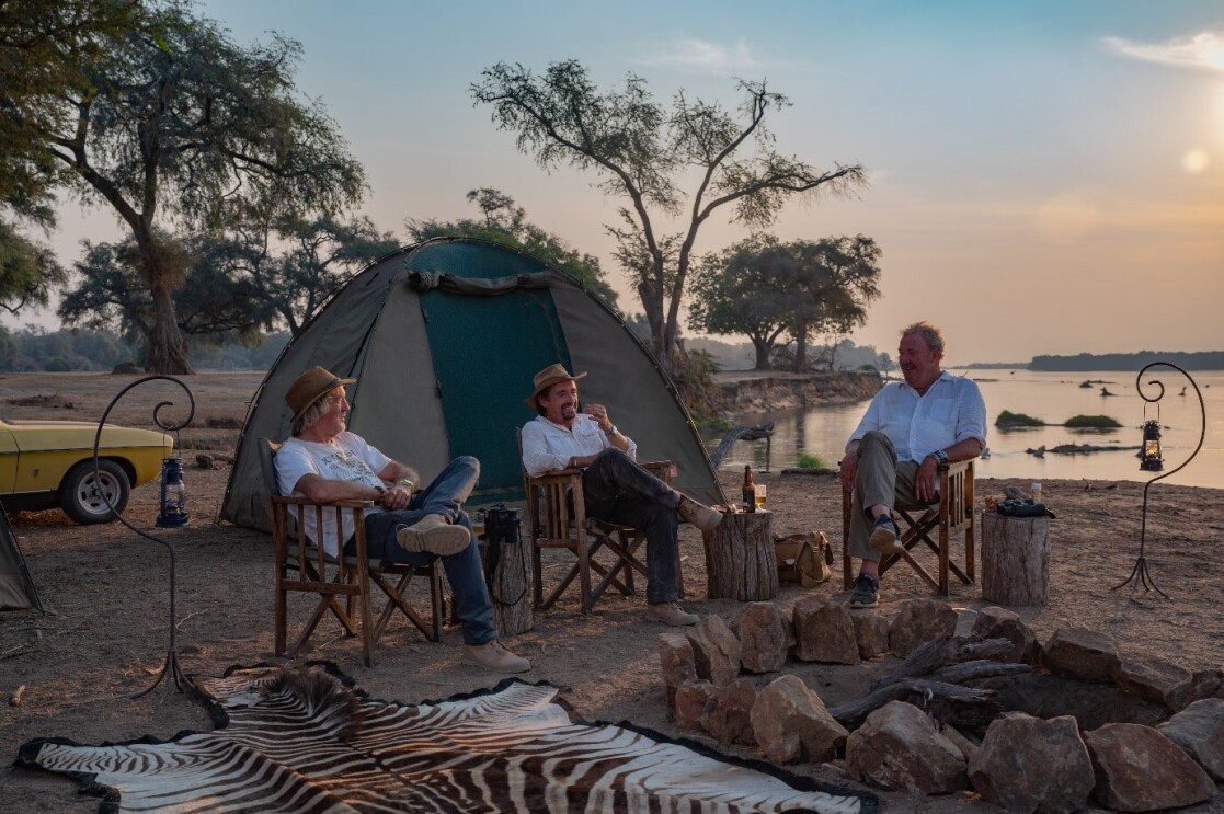 A screenshot from The Grand Tour featuring James May, Richard Hammond, and Jeremy Clarkson sat next to a tent