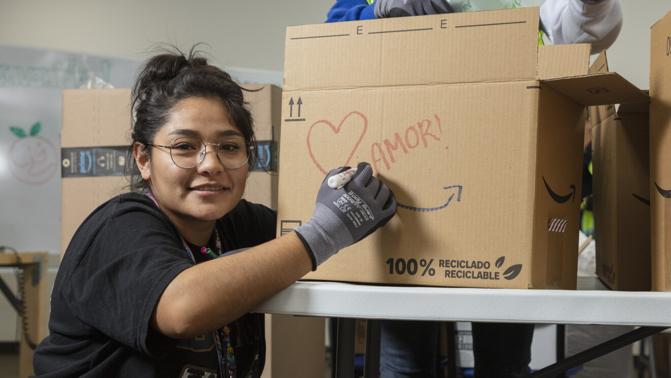 Trabajadora de un centro logístico de Amazon escribiendo la palabra Amor en una caja que pone 100 % reciclado. 