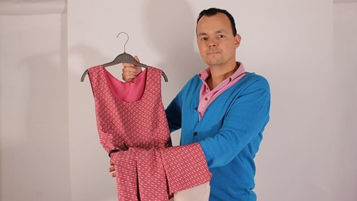 IUn homme tient dans ses mains une robe rose Oxalla sur un cintre