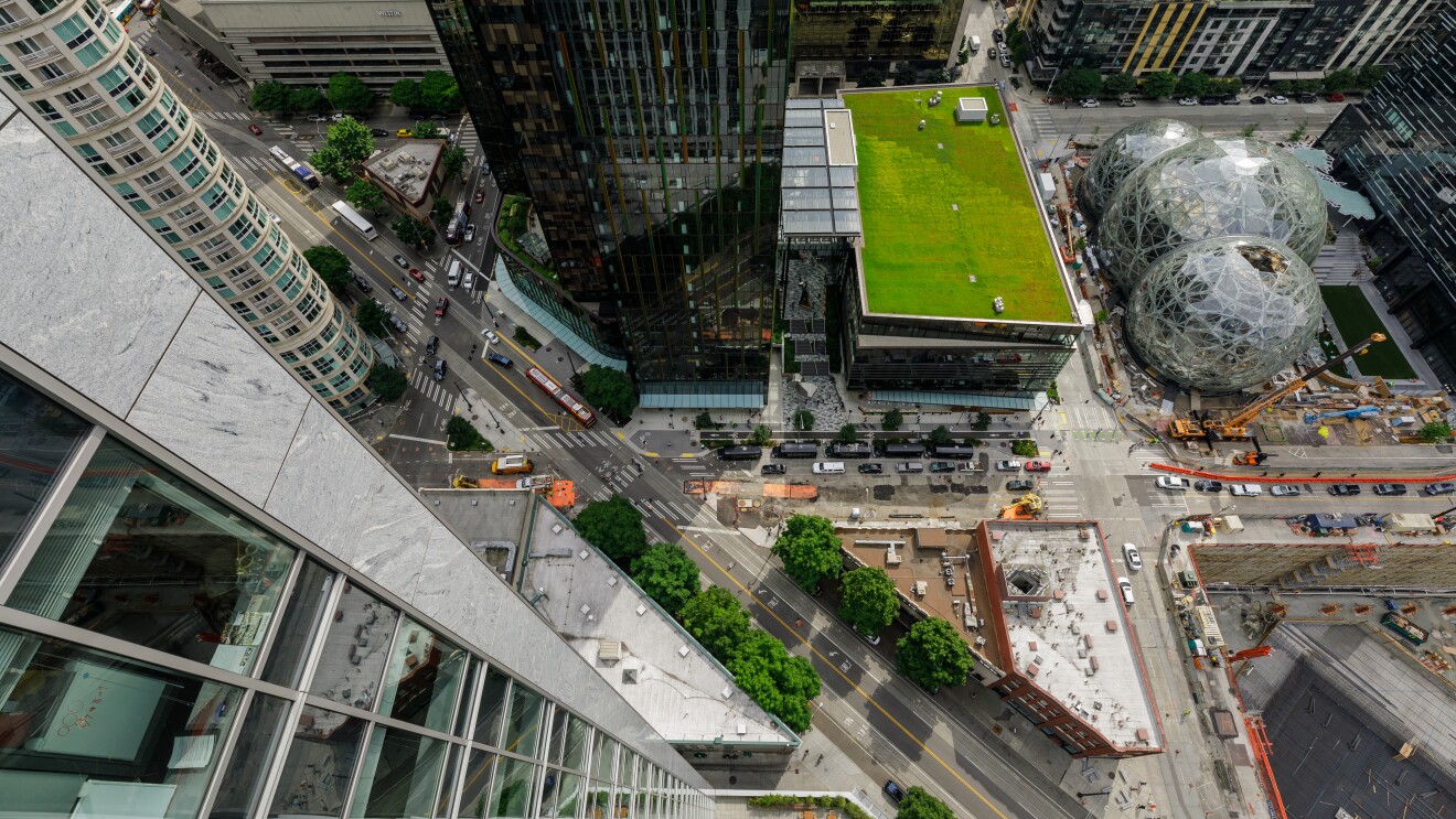 一个视图从摩天大楼之上,俯视着亚马逊校园的发展。起重机操作员指导机械附近的亚马逊球体。汽车开在城市的街道上。