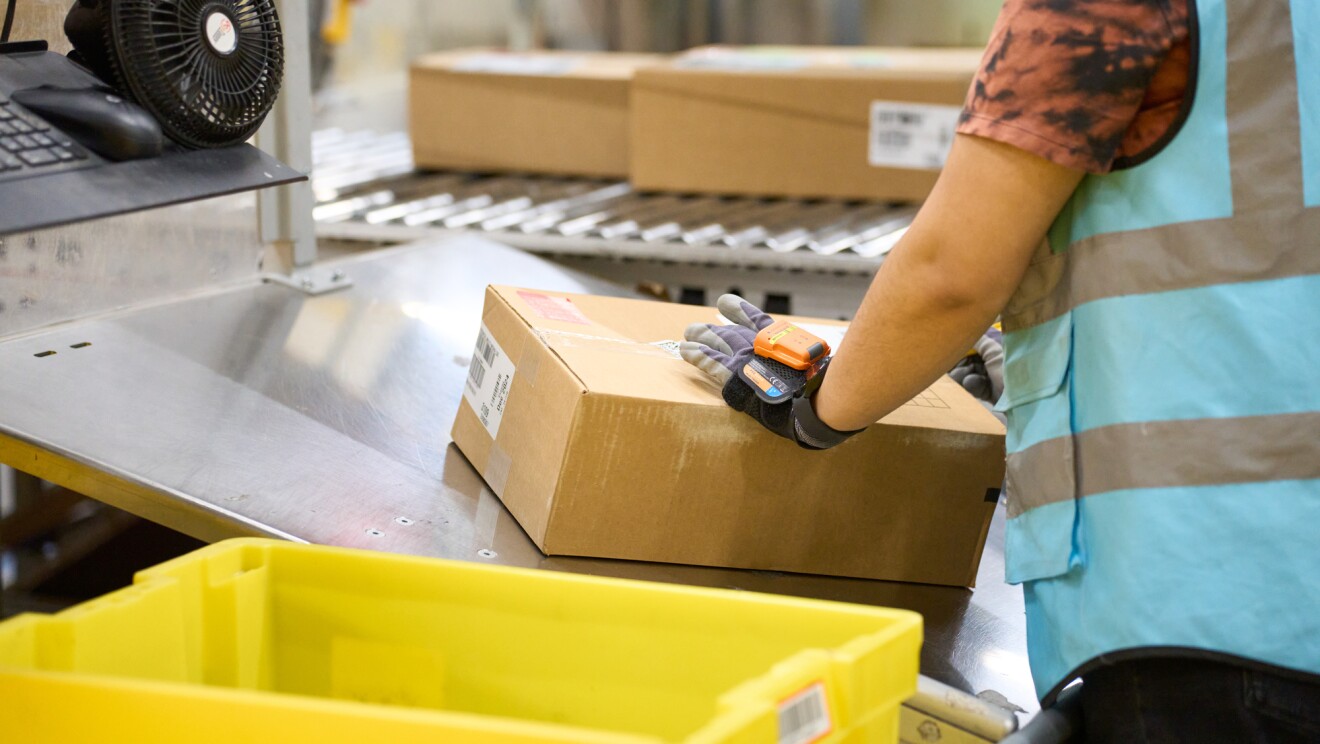 An Amazon fulfillment centre employee scanning a package on a conveyor belt
