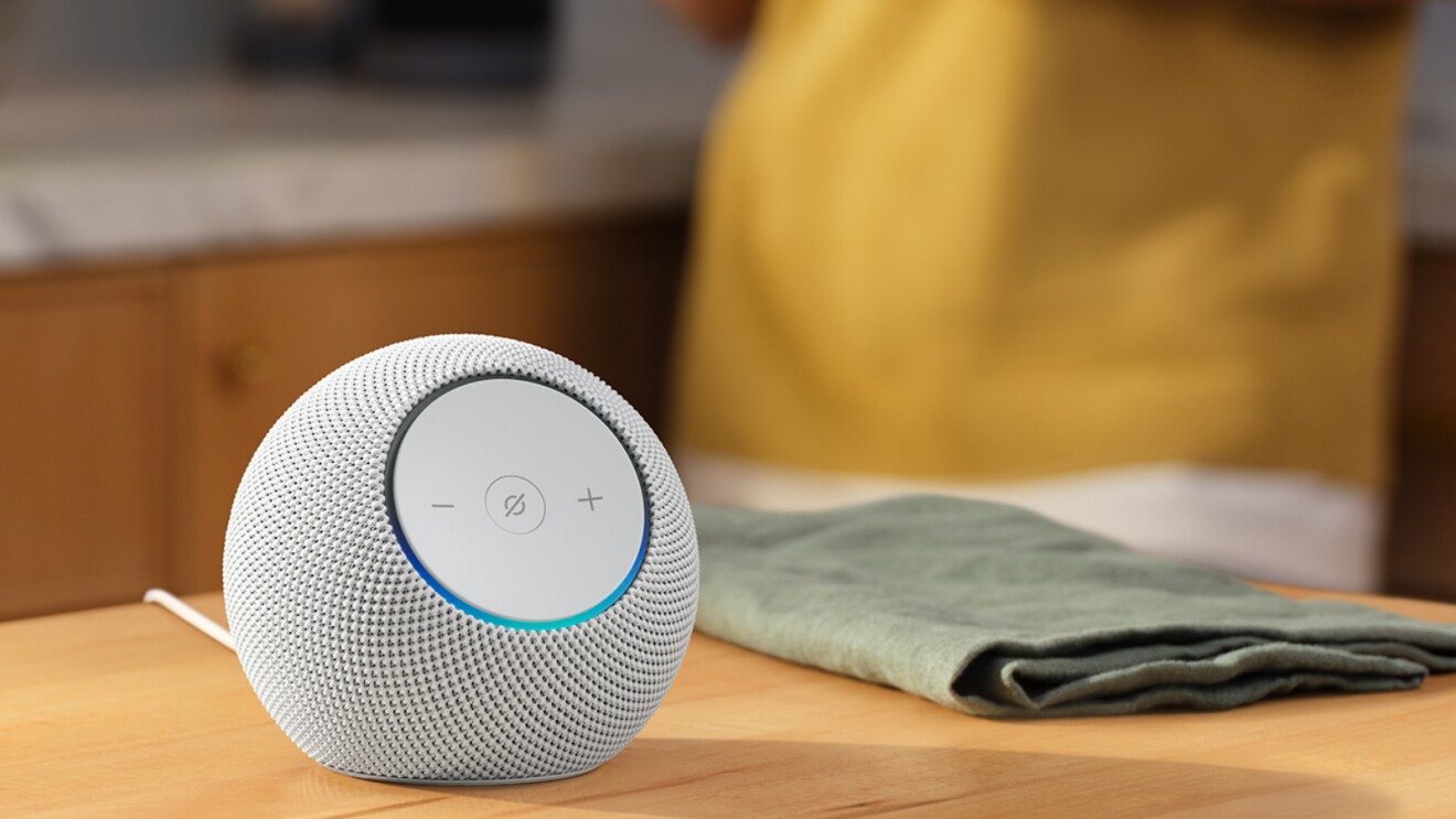 Amazon Echo White on a Kitchen counter next to a Green kitchen cloth, with a woman wearing a yellow bib