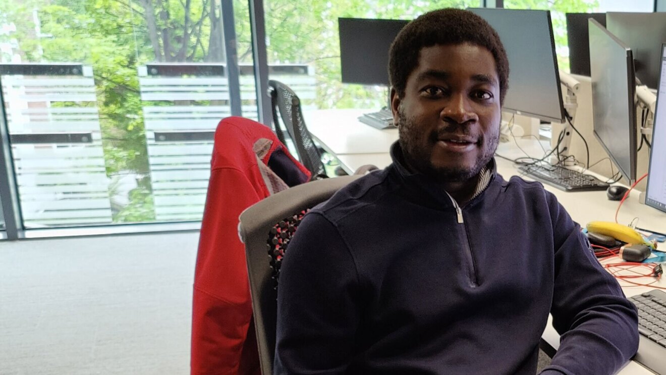 一名男子坐在办公室的办公桌前微笑着拍照。