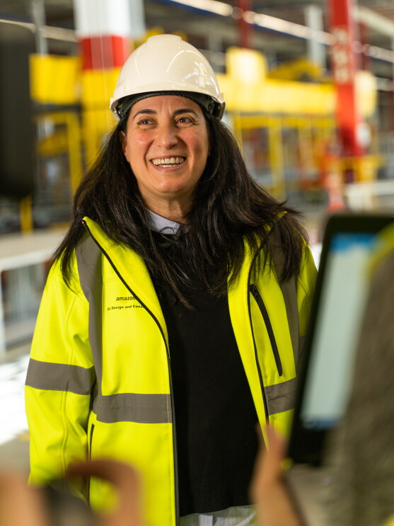 Sonia Corvera, Responsable Senior de Construcción para Amazon España, en primer plano y sonriendo con casco y chaleco amarillo. En un momento de la grabación. 