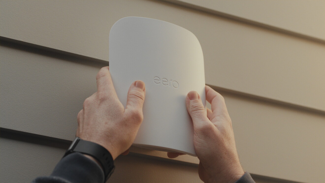 Hands installing Eero WiFi router on wall