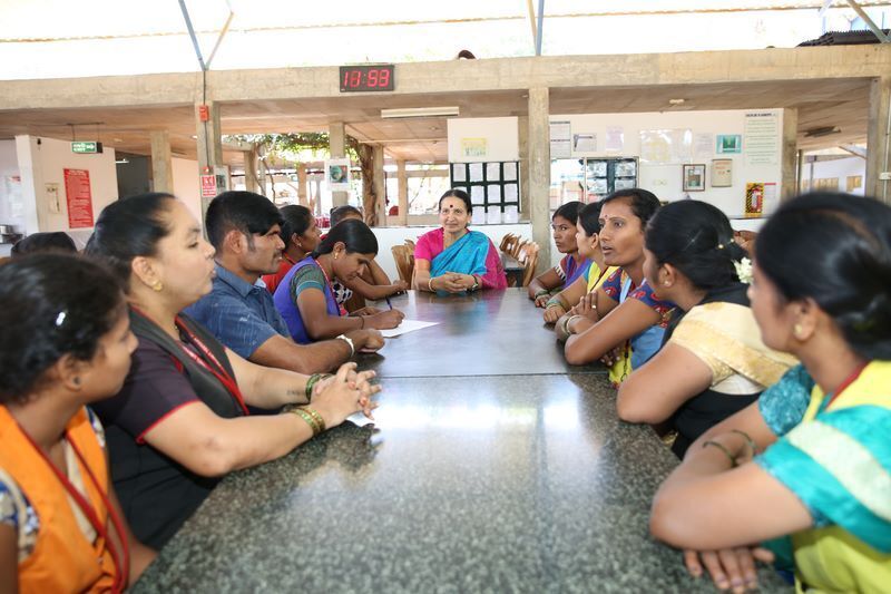 A couple of women and men wearing Indian traditional clothes are sitting around a long table