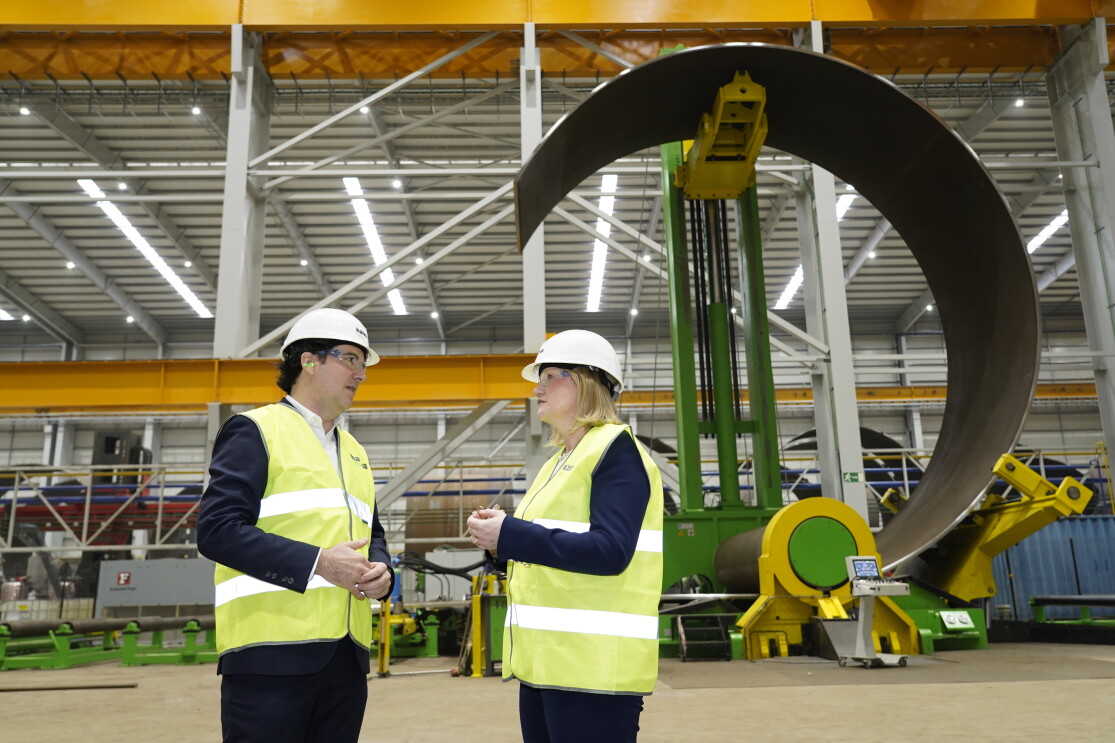 A man and a woman wearing hard hats and hi-vis jackets survey a warehouse site