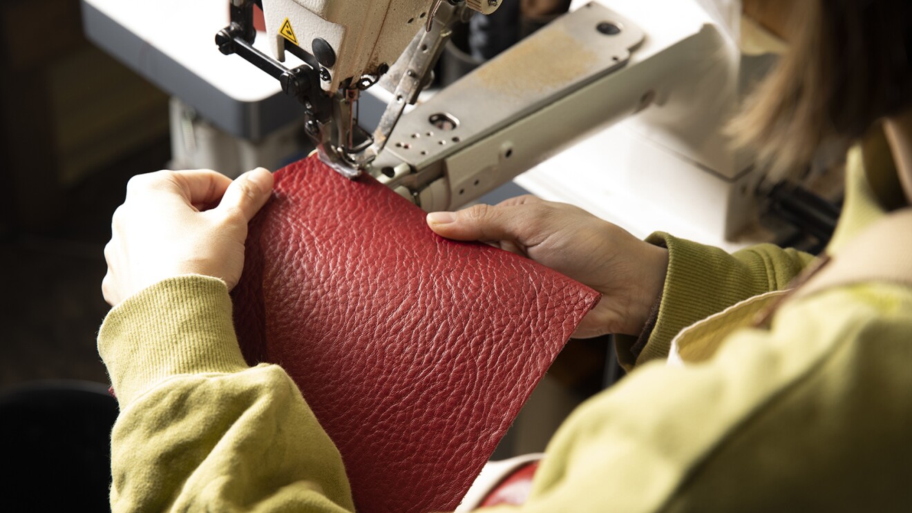 赤い革をミシンで縫っている職人の手