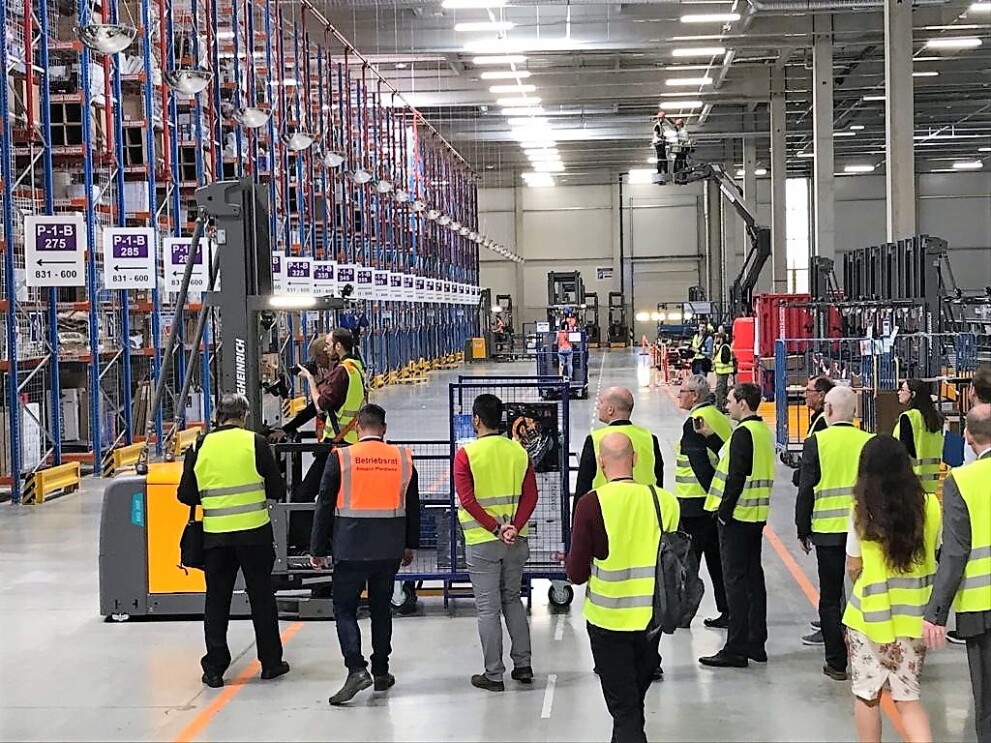 Ein Dutzend Besucher in gelben Sicherheitswesten in einem Hochregallager