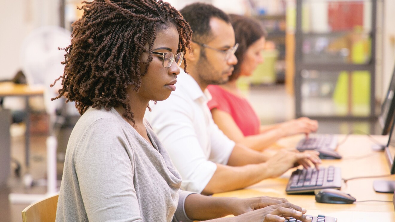 A photo of three employees working on desktop computers in a digital skills training.