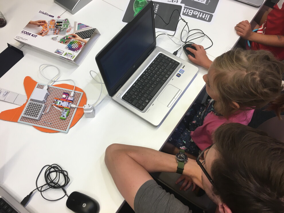 Ein junges Mädchen sitzt am Computer und programmiert. Neben sitzt ein Amazon Mitarbeiter, der ihr hilft und das Programmieren erklärt.