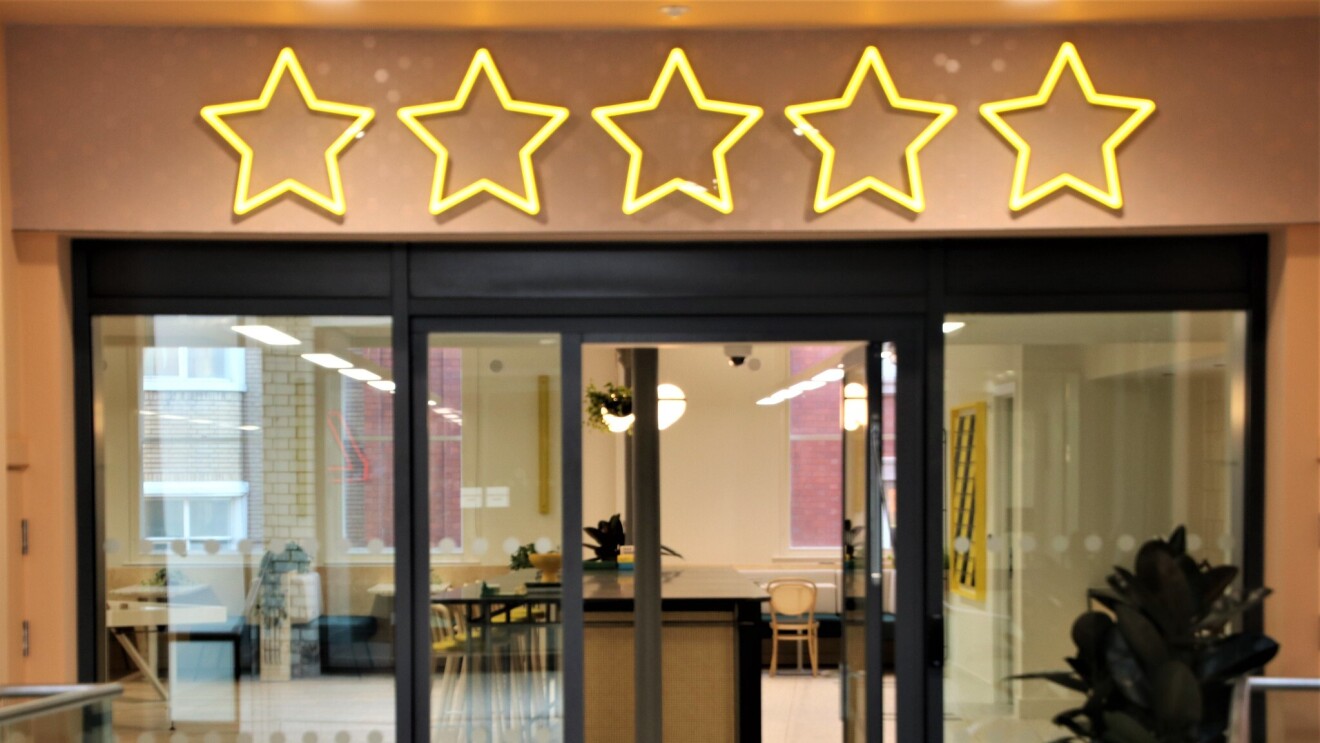 A view of the break area in the Amazon Manchester offices, this is viewed from outside of the open doors. Above the doors are neon lights depicting five stars.
