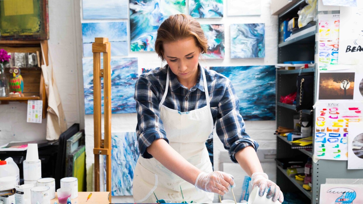 Kate Chesters creating a resin board using blue, red, purple and white resins. She working from her Liverppool based studio and there are lots of her artworks surrounding her.