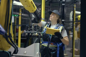 An Amazon employee wears safety gear and works with a robot in a fulfillment center.