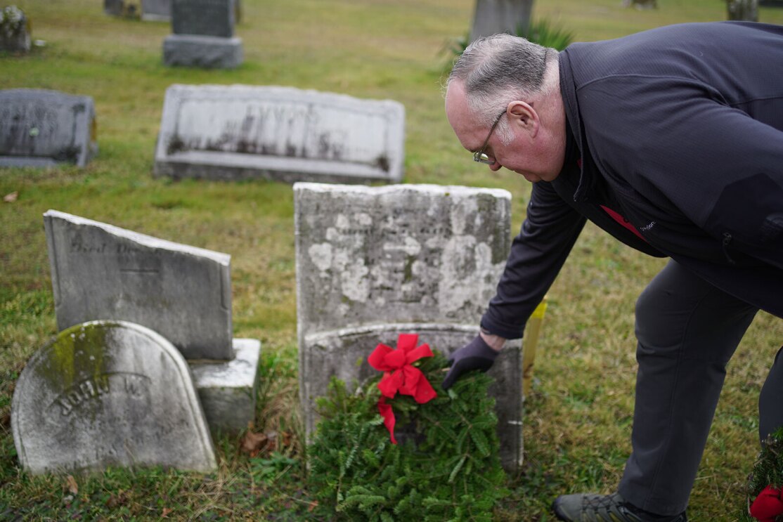 An image of Clint placing a wreath and a flag on the grave of a veteran.