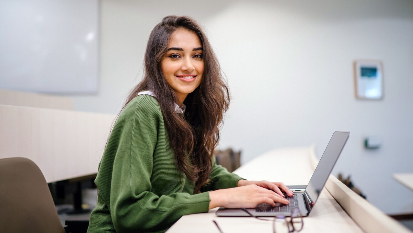 一名年轻女子穿着一件绿色的运动衫对着镜头微笑在研究她的笔记本电脑。
